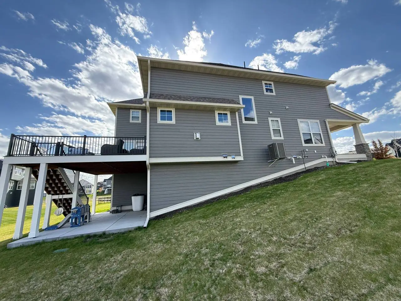 Comprehensive custom seamless gutter system and complex downspout routing on a sloped residential property with a walkout basement in Delano.