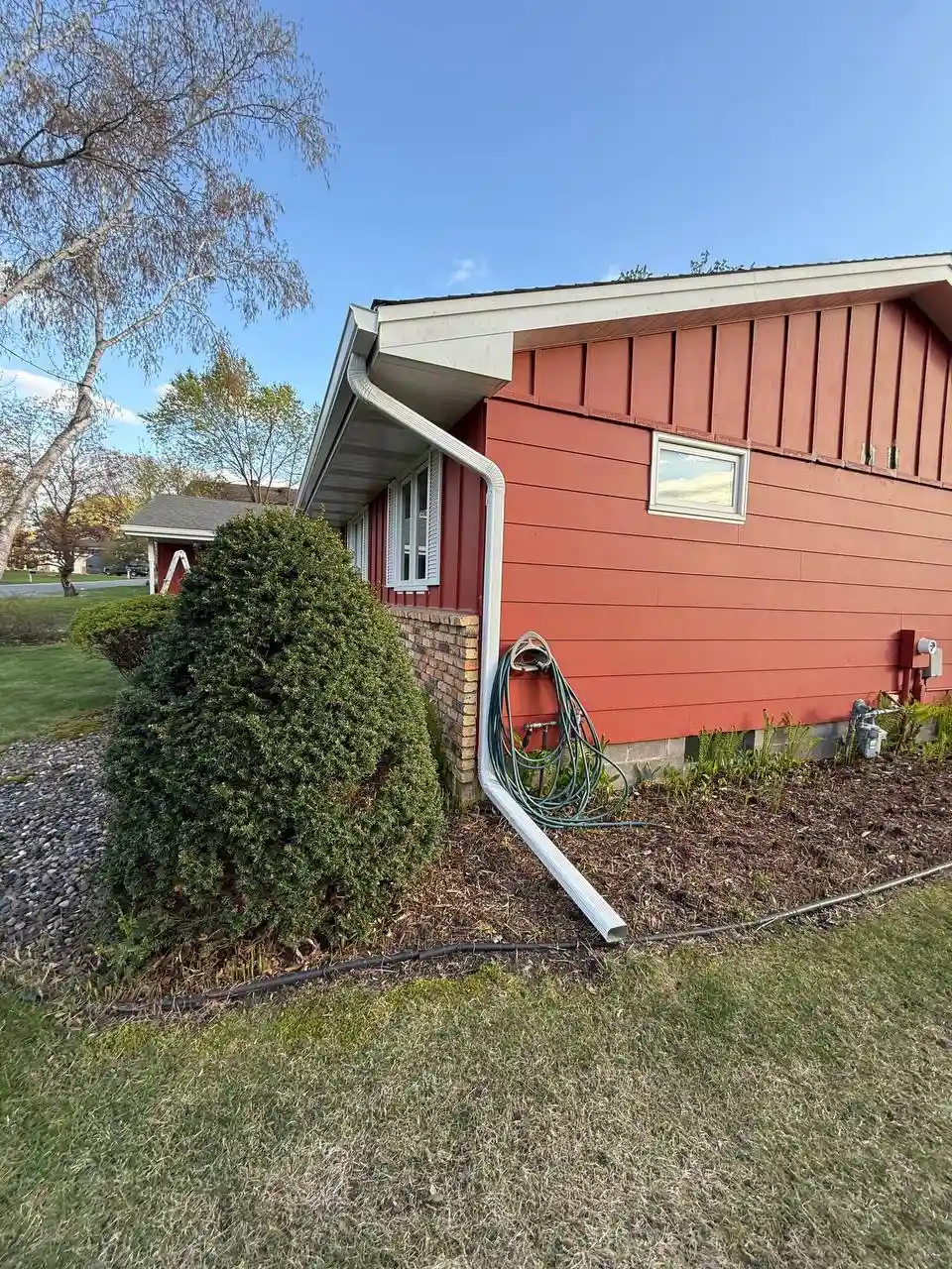 Close-up of downspout routed around roof overhang with mulch bed extension in Eden Prairie