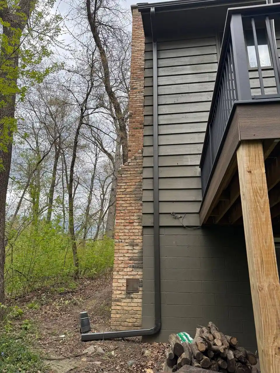 Dark brown custom downspout neatly installed next to a brick chimney, protecting the home's foundation in Eden Prairie.