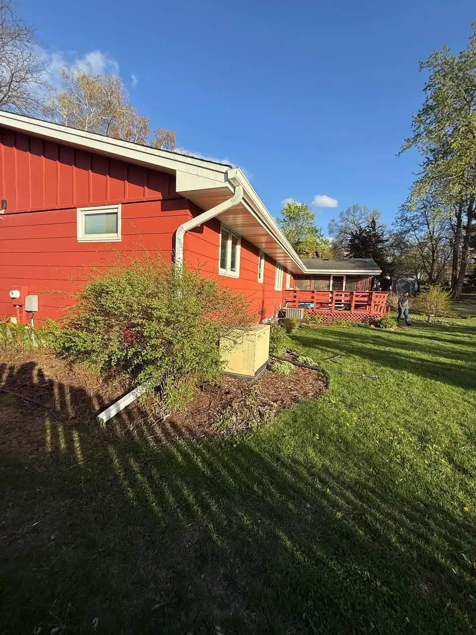 White seamless gutters and downspout extension protecting landscaping and a standby generator on a red home in Eden Prairie.