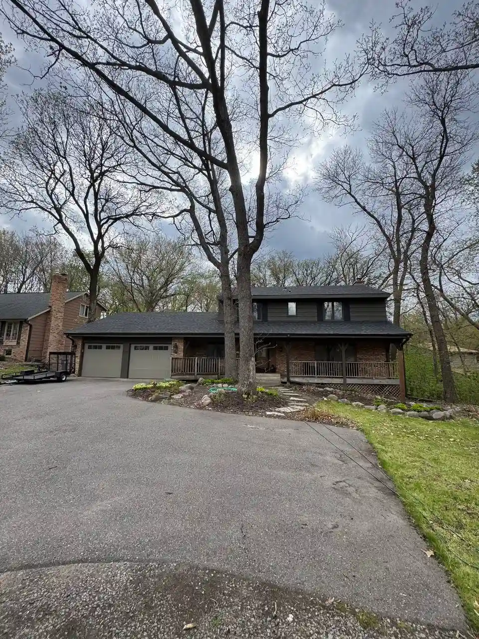 Wide front exterior view of a large home in Eden Prairie featuring a complete dark seamless gutter installation on a heavily wooded lot.