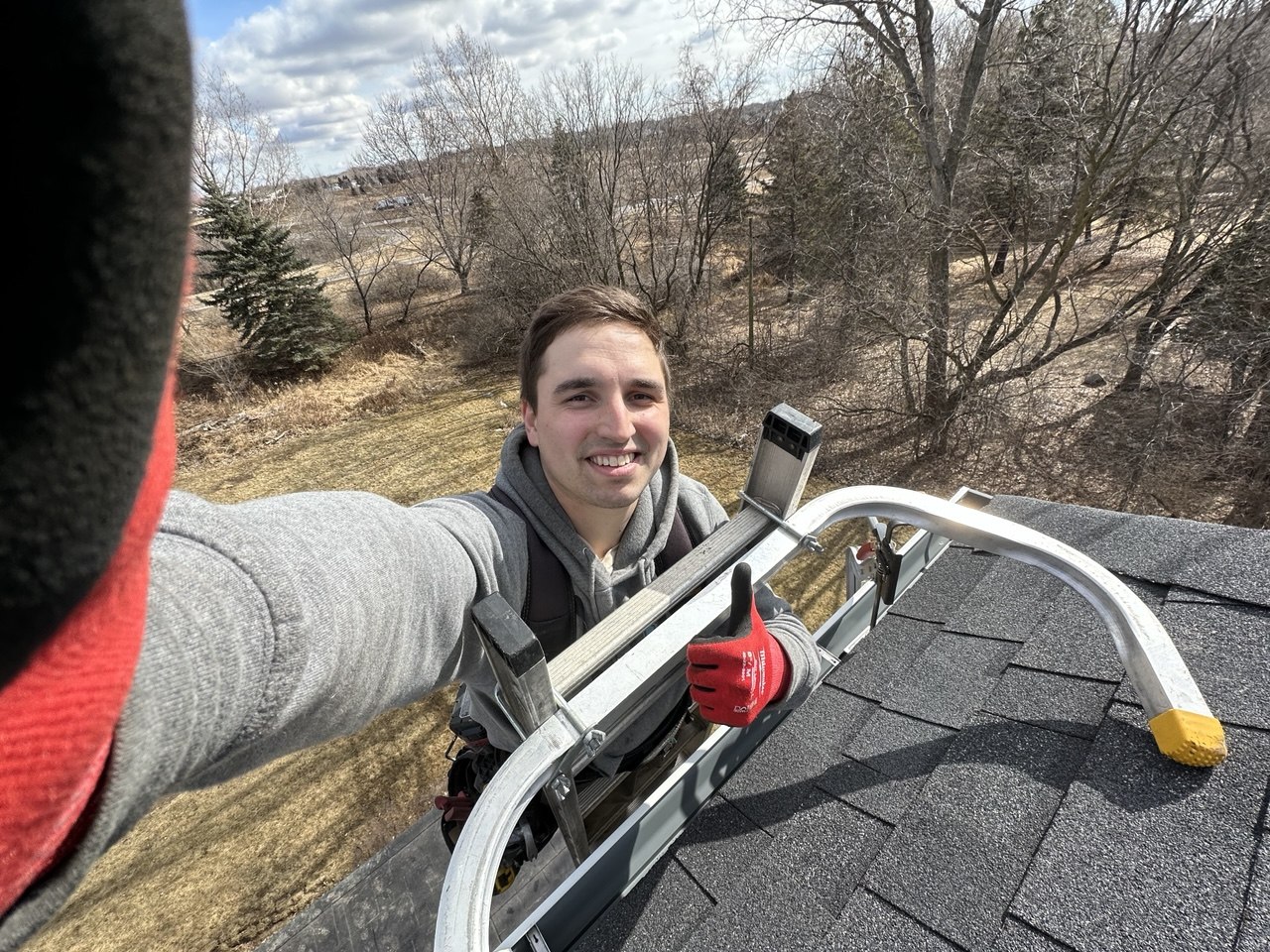 Vitalii on a rooftop giving thumbs up while installing gutters